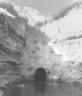 On old black and white photo of a tunnel with water surrounded by cliffs.